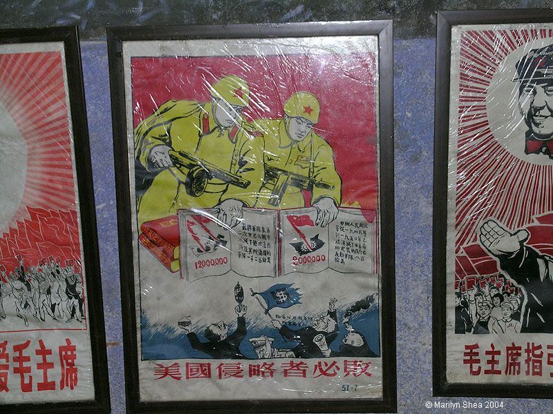 another view - Poster shows two PLA soldiers behind a stack of Little Red Books holding machine guns pointed at small people below waving a flag with a dollar sign on it