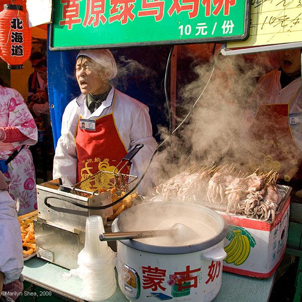 Squid on sticks ready for cooking with the vendor shouting to the crowd