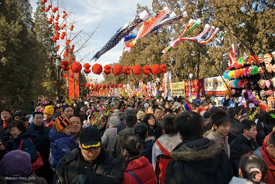 The crowd along a pathway below flying windsocks and lanterns