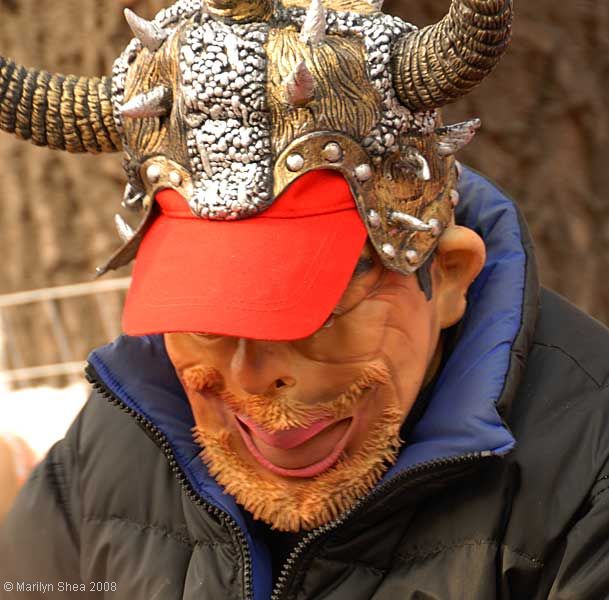 Man with a monster mask and a set of horns put on over his red baseball hat