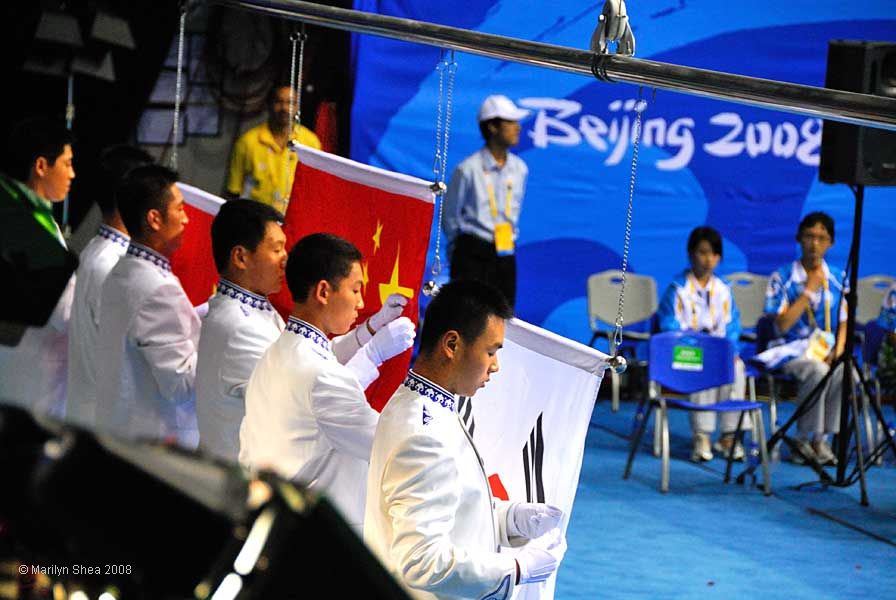 Two Chinese and a Korean Flag are hed by three ushers waiting to raise them