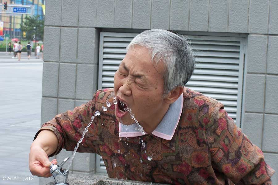 Woman drinking water from a large stone water fountain