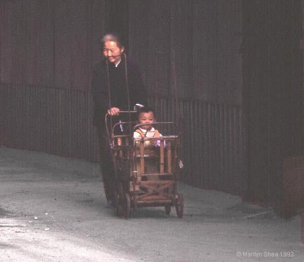 child in a bamboo baby carriage pushed by a grandmother