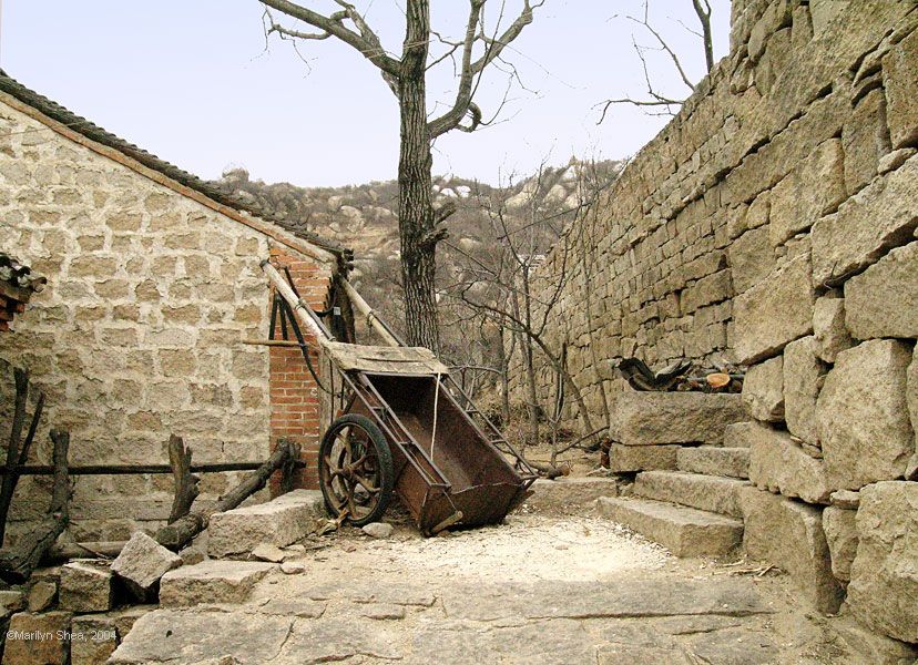 Donkey cart with metal bin resting against stone building